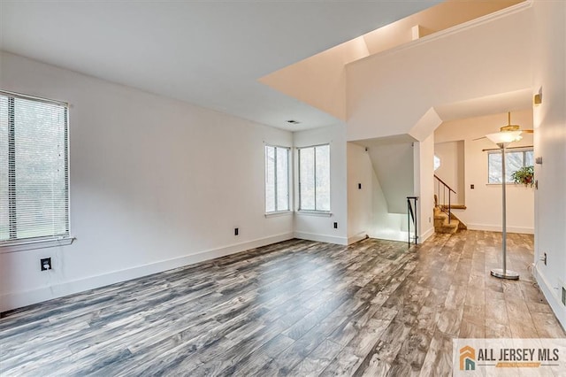 unfurnished living room with stairway, baseboards, and wood finished floors