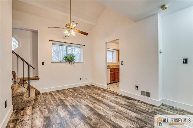 unfurnished living room featuring visible vents, ceiling fan, stairway, light wood-style flooring, and vaulted ceiling