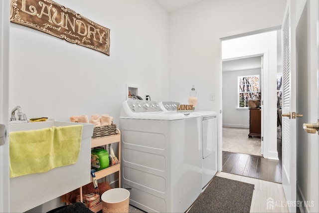 clothes washing area with laundry area, wood finished floors, baseboards, separate washer and dryer, and a sink