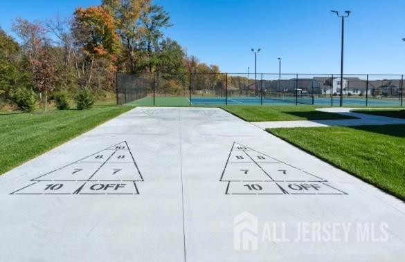 view of community with fence, a yard, shuffleboard, and a tennis court