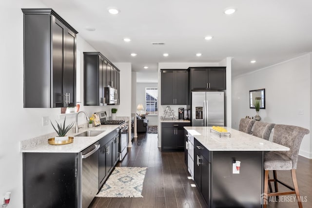 kitchen with ornamental molding, a kitchen island, light stone countertops, a sink, and appliances with stainless steel finishes