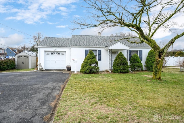 single story home featuring a garage, driveway, a shingled roof, a storage unit, and a front lawn