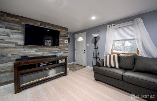 living room with baseboards, a glass covered fireplace, an accent wall, light wood-type flooring, and recessed lighting