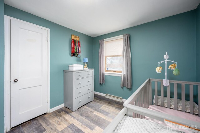 bedroom with a baseboard radiator, a nursery area, and hardwood / wood-style floors