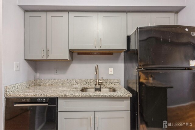 kitchen with light stone countertops, dishwasher, freestanding refrigerator, and a sink