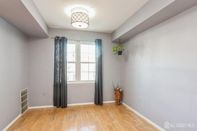 spare room featuring light wood-type flooring, visible vents, and baseboards