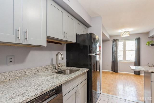 kitchen with a sink, baseboards, freestanding refrigerator, light stone counters, and light tile patterned floors