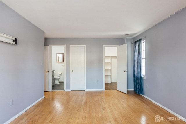 unfurnished bedroom with ensuite bathroom, visible vents, baseboards, a spacious closet, and light wood-style floors