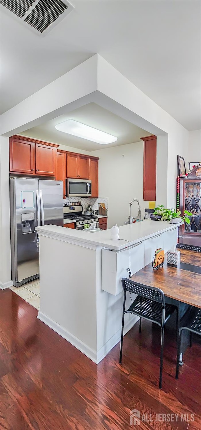 548 E Celebration Way E, South Plainfield, NJ 07080 - kitchen featuring appliances with stainless steel finishes, light wood finished floors, a peninsula, tasteful backsplash, and light countertops