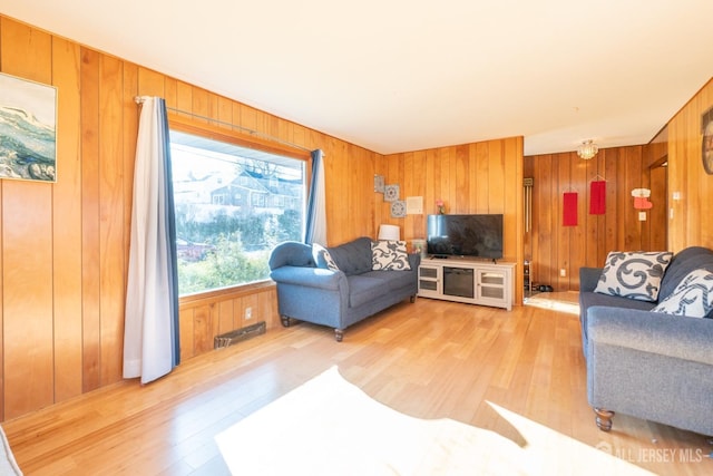 living area with light wood-type flooring, visible vents, and wooden walls