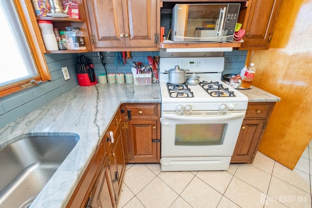 kitchen featuring stainless steel microwave, gas range gas stove, brown cabinetry, and decorative backsplash