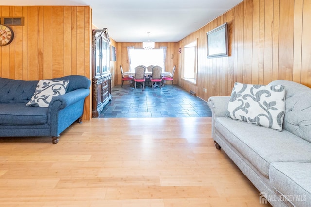 living area featuring light wood-style flooring, wooden walls, visible vents, and a notable chandelier