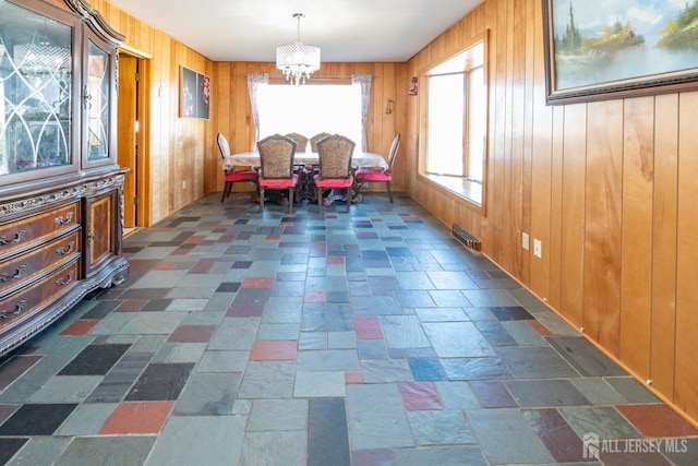 dining area with stone finish floor, visible vents, wood walls, and a notable chandelier