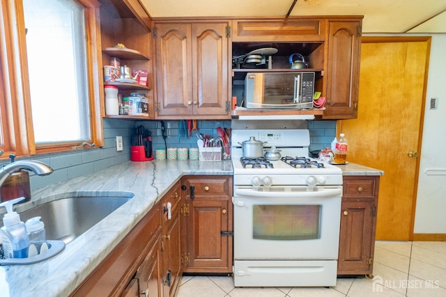 kitchen featuring a sink, brown cabinetry, open shelves, stainless steel microwave, and white gas range