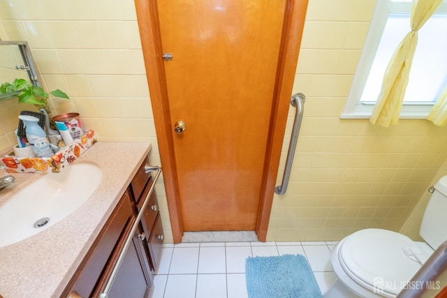 half bath with toilet, vanity, tile walls, and tile patterned floors