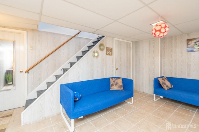 living area with stairs, tile patterned floors, a paneled ceiling, and wooden walls