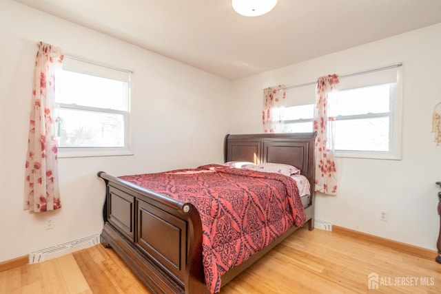 bedroom with light wood-style flooring, a baseboard heating unit, and baseboards