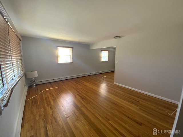 spare room featuring a baseboard radiator, baseboards, and wood finished floors