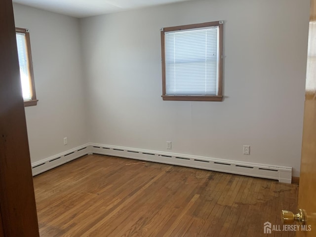 unfurnished room featuring a baseboard heating unit and hardwood / wood-style floors