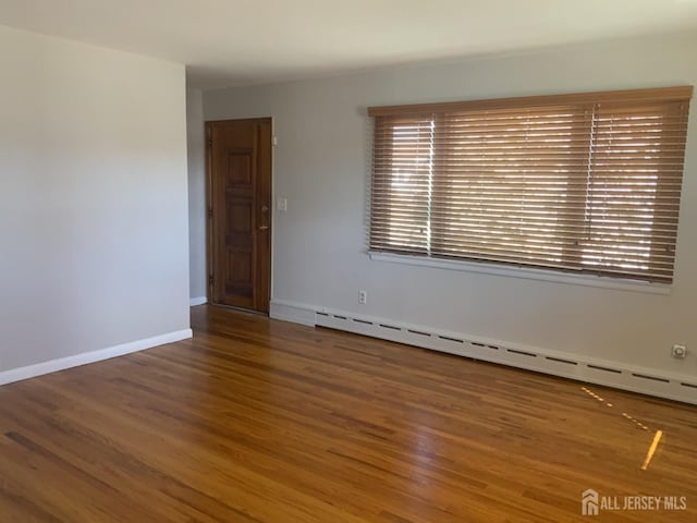 spare room with baseboards, baseboard heating, and wood finished floors