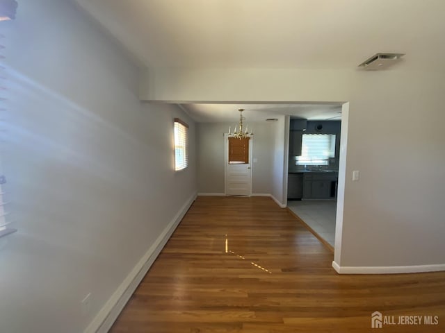 hall with a notable chandelier, wood finished floors, and baseboards