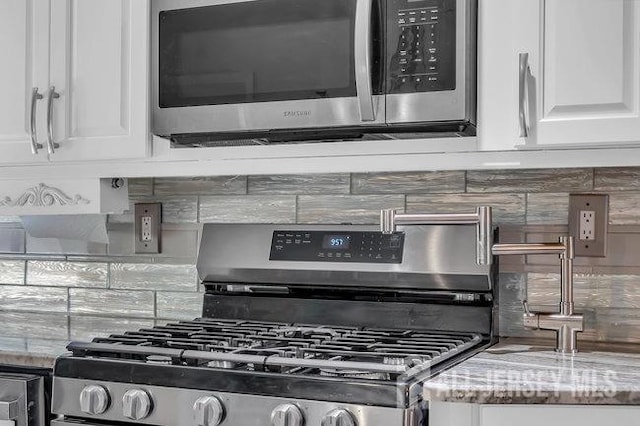 interior space featuring appliances with stainless steel finishes, white cabinetry, backsplash, and light stone counters