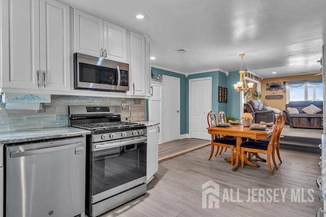 kitchen featuring stainless steel appliances, light hardwood / wood-style flooring, an inviting chandelier, tasteful backsplash, and white cabinets