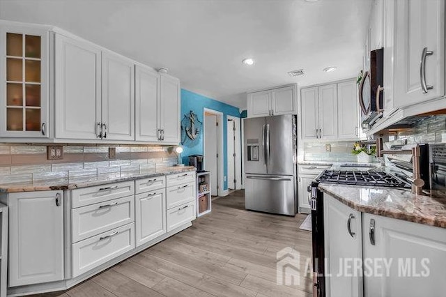 kitchen featuring light hardwood / wood-style flooring, backsplash, light stone counters, white cabinetry, and stainless steel appliances