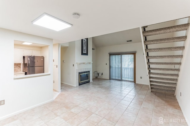 unfurnished living room with light tile patterned floors, visible vents, baseboards, stairs, and a tiled fireplace