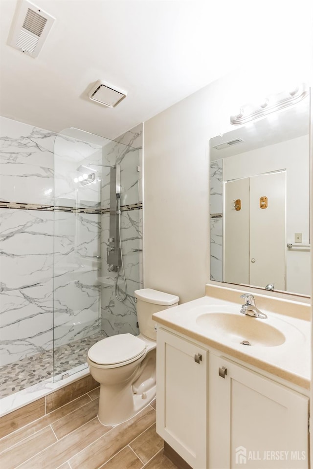 full bath with a marble finish shower, visible vents, toilet, wood tiled floor, and vanity