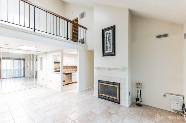 unfurnished living room with high vaulted ceiling, a tile fireplace, visible vents, and baseboards