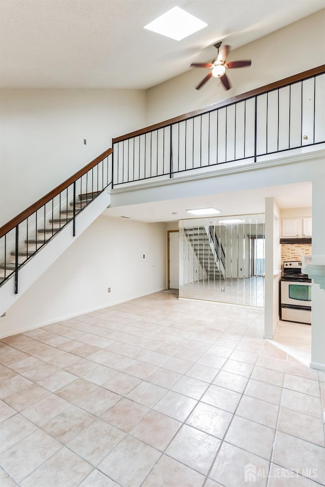 unfurnished living room featuring a skylight, stairway, a towering ceiling, a ceiling fan, and light tile patterned flooring