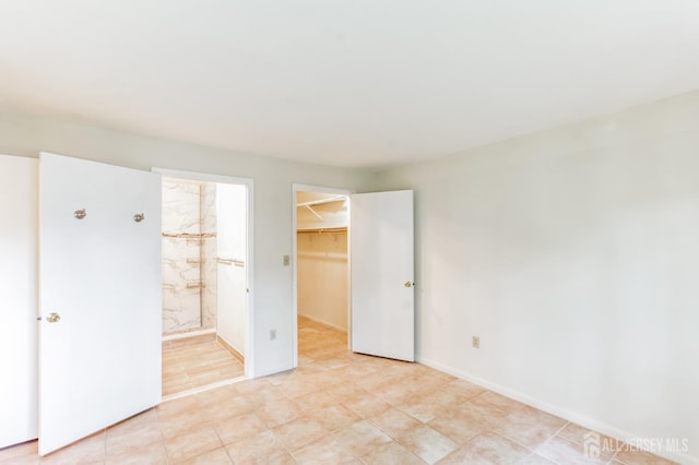 unfurnished bedroom featuring a spacious closet, a closet, ensuite bath, and baseboards