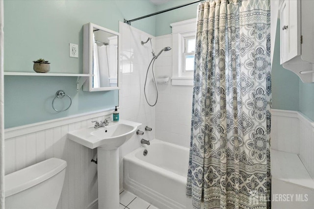 bathroom with a wainscoted wall, toilet, shower / bath combo with shower curtain, a sink, and a decorative wall