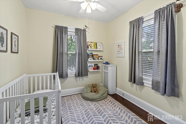 bedroom with multiple windows, wood finished floors, a crib, and baseboards