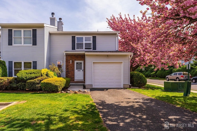 view of front of home with a chimney, a front yard, an attached garage, and driveway