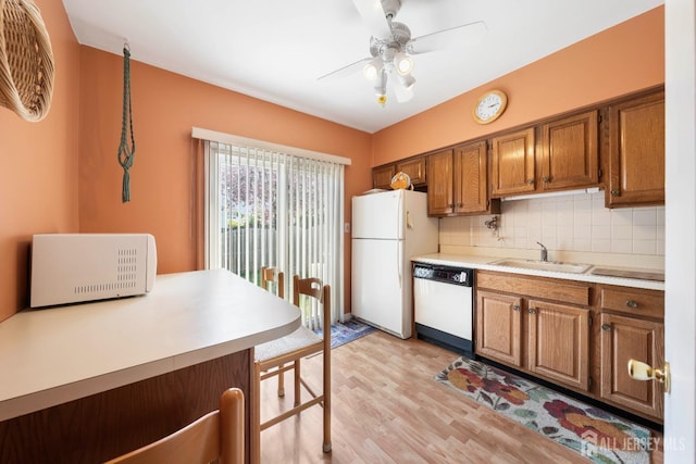 kitchen with light wood-style flooring, white appliances, a sink, brown cabinets, and tasteful backsplash