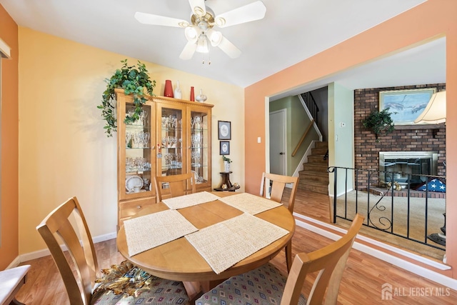 dining room featuring a fireplace, light wood-style flooring, stairs, and a ceiling fan