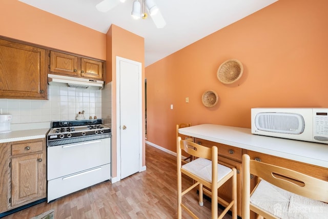 kitchen with brown cabinets, range with gas cooktop, white microwave, under cabinet range hood, and decorative backsplash