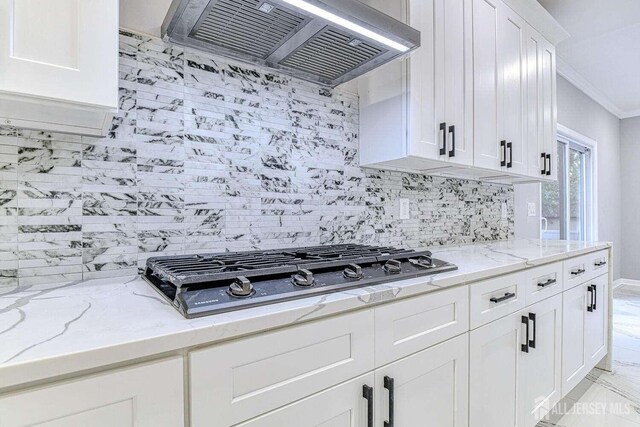 kitchen with backsplash, white cabinets, light stone countertops, range hood, and gas cooktop