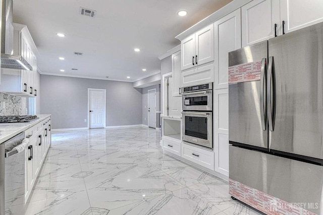 kitchen with light stone countertops, wall chimney range hood, appliances with stainless steel finishes, white cabinets, and ornamental molding