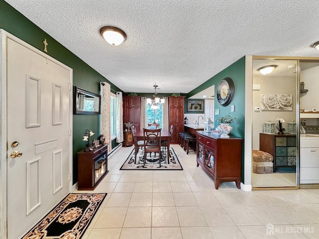 interior space with a textured ceiling, light tile patterned floors, an inviting chandelier, a sink, and washer / dryer