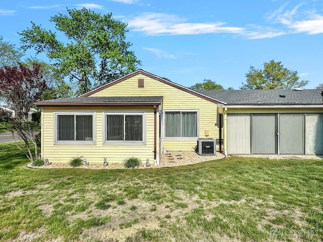 rear view of property with central air condition unit and a yard