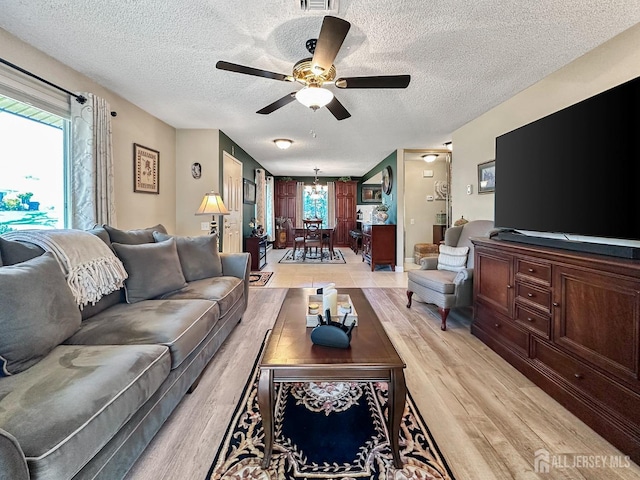living area featuring a healthy amount of sunlight, light wood finished floors, a textured ceiling, and ceiling fan with notable chandelier