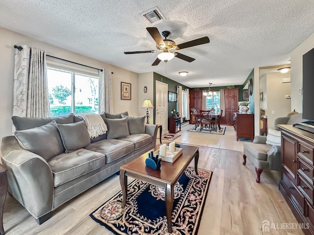 living room featuring light wood-type flooring, visible vents, a textured ceiling, and ceiling fan with notable chandelier