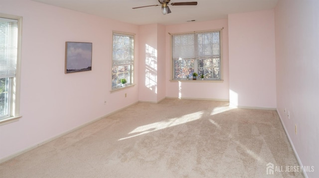 carpeted spare room featuring a ceiling fan, a wealth of natural light, visible vents, and baseboards