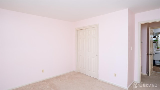 unfurnished bedroom with a closet, light carpet, and baseboards