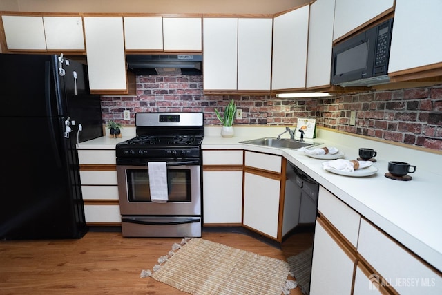 kitchen featuring light countertops, white cabinets, a sink, under cabinet range hood, and black appliances