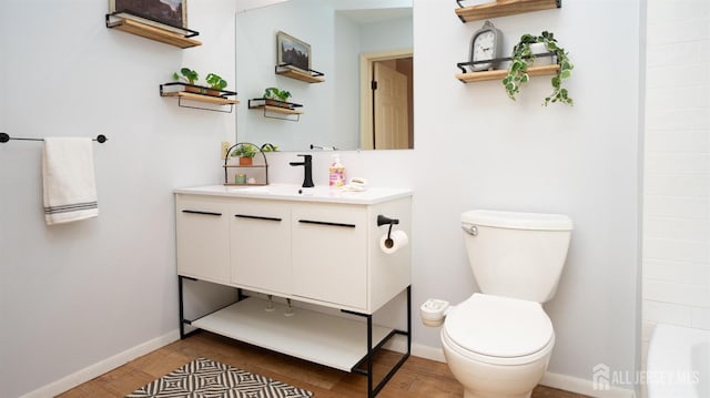 bathroom featuring baseboards, toilet, wood finished floors, vanity, and a bath