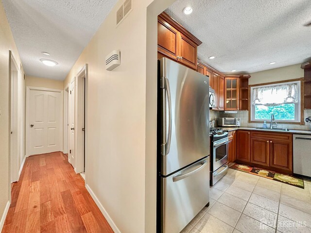 12 Dana Estates Dr, Old Bridge, NJ 08859 - kitchen with stainless steel appliances, a textured ceiling, brown cabinetry, a sink, and tasteful backsplash